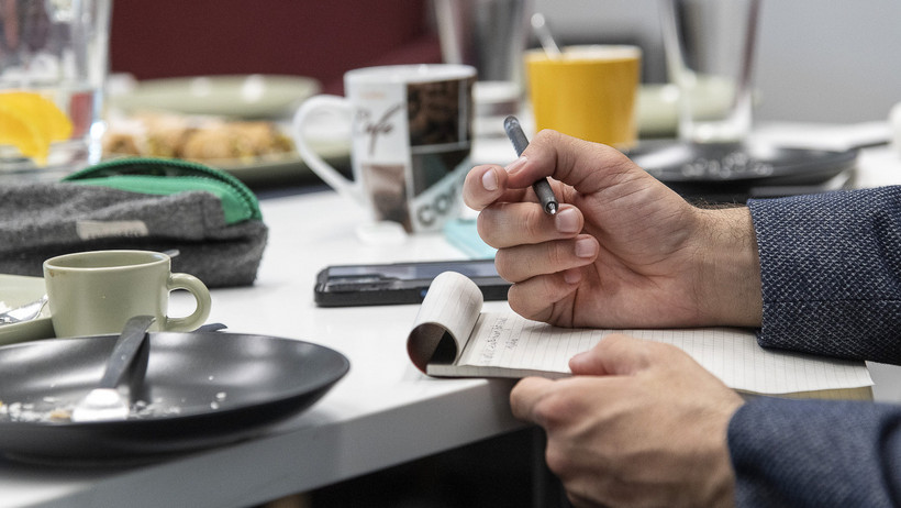 Notizen werden auf ein Blatt geschrieben, auf dem Tisch Kaffeegeschirr