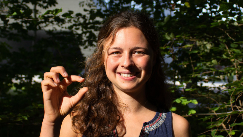 Studentin Pia Bradler zeigt mit ihrer Hand die Größe der Flechten an, die sie auf dem Feld gezählt hat.