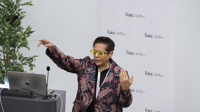 A picture of South African poet Yvette Christiansë gesturing while explaining something. Behind her is a sign reading lias: Culture and Society