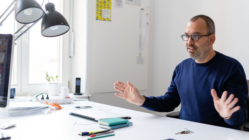 The cultural scientist Andreas Bernhard sits in his office and explains something.