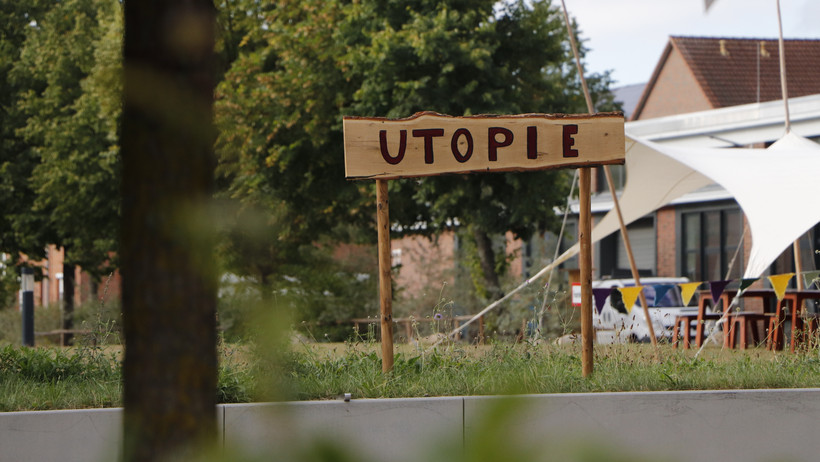 Ein Schild mit der Aufschrift "Utopie" vorm Zentralgebäude der Leuphana