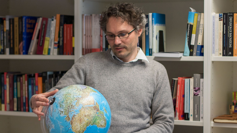 Prof. Dr. Tobias Lenz betrachtet einen Globus. 