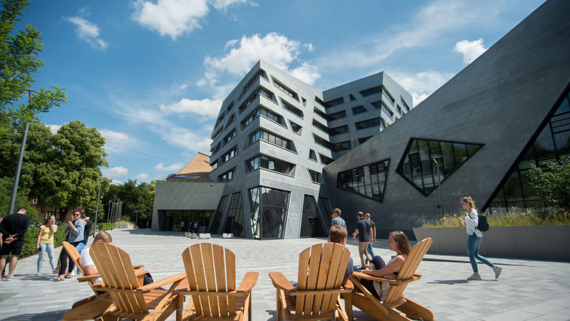 Four wooden chairs on the lively front square of Leuphana University's central building