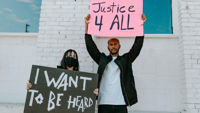  Zwei junge Menschen halten Plakate hoch. Darauf steht “I want to be heard” und “Justice 4 all”.