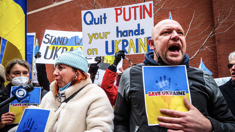 Auf dem Bild sind drei demonstrierende Personen zu sehen. Sie halten Schilder mit der Beschreibung “Save Ukraine” hoch und rufen etwas.