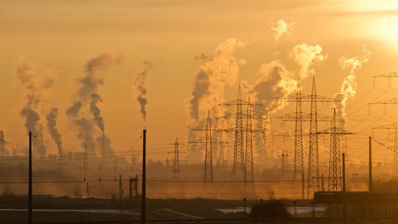 Ein Industriegebiet mit Emissionswolken und Strommasten vor einem orangenen Sonnenuntergang