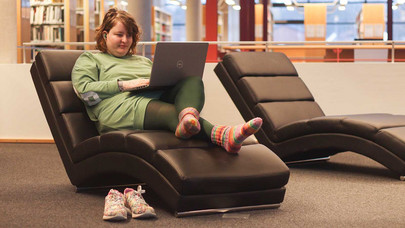 Eine Studentin mit Laptop auf einer Relax Liege in der Bibliothek