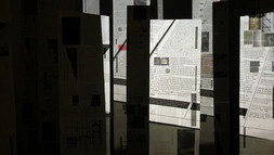 [Translate to Englisch:] Wie Skulpturen verteilen sich die Papierbahnen im Kunstverein Lüneburg, auf ihnen die Projektion einer durch die Zeitung blätternden Hand. 