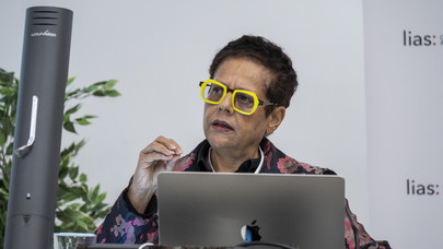 A photograph of South African poet Yvette Christiansë, wearing yellow-brimmed glasses, with a laptop infront of her