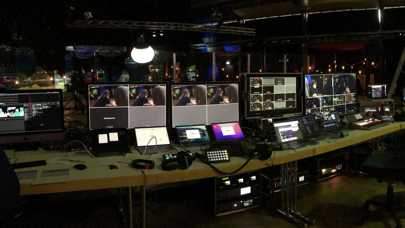Das Foto zeigt eine Reihe von Computern und Bildschirmen, die auf Tischen vor der Bühne des Studios der Konferenzwoche stehen.