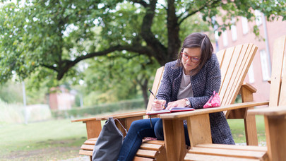 A student is working in a wooden chair on campus.