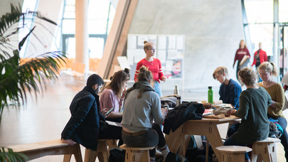 Eine Gruppe Studierender sitzt um einen Tisch im Foyer des Zentralgebäudes.