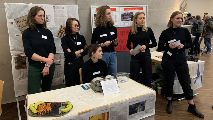 Studierende präsentieren an ihrem Stand ihren Vortrag, beginnen Diskussionen mit ihren Gästen und verteilen ein paar Snacks und Sticker.