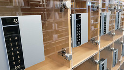 Eine Reihe Schliessfaecher aus Buchenholz mit gläsernen Türen und je einem PIN Code Bedienfeld