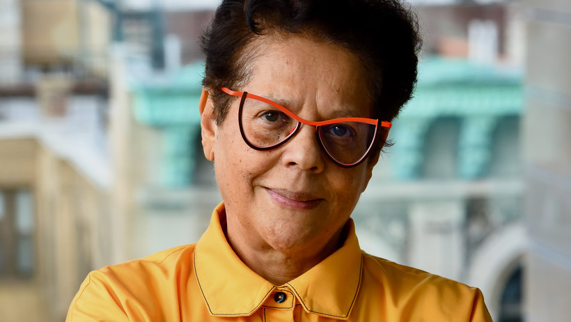 A portrait photo (Head and shoulders) of south African poet Yvette Christiansë, wearing a yellow dress shirt and glasses with a red brim