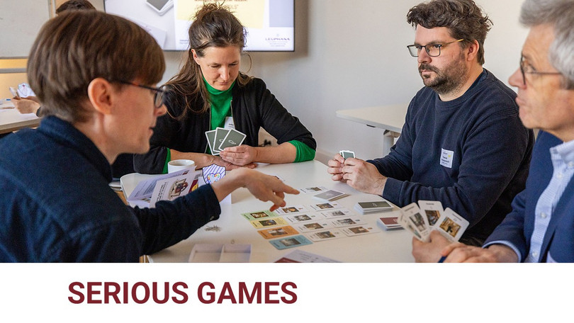 Serious Games für die Schulentwicklung Vier Menschen sitzen an einem Tisch und spielen ein Kartenspiel