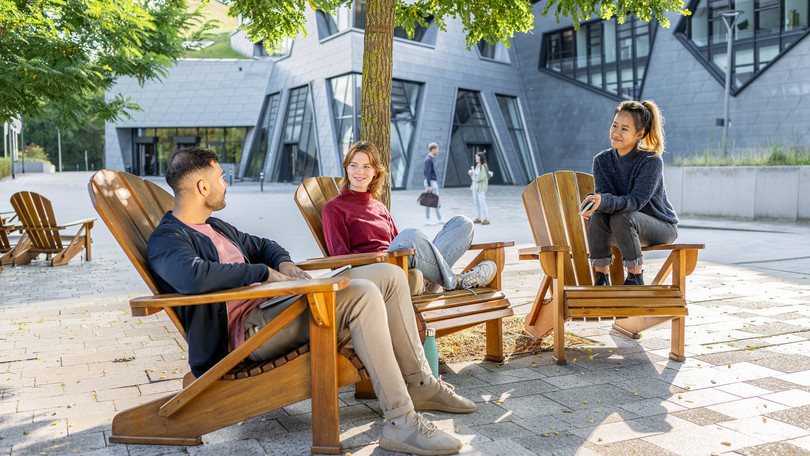 Gespräch von Studierenden des Master Cultural Studies auf den Stühlen vorm Zentralgebäude
