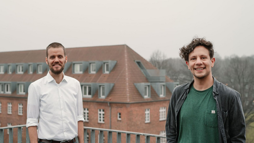 Der Psychologe Prof. Dr. David Loschelder und Betriebswirt Dr. Meikel Soliman stehen auf dem Balkon eines Campusgebäudes.