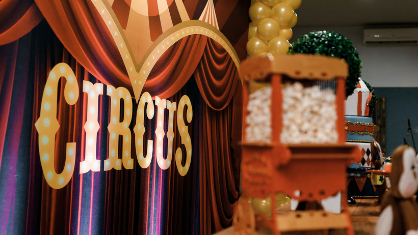 Es sind eine Zirkusarena mit der leuchtenden Aufschrift “Circus” und eine Popcornmaschine zu sehen.