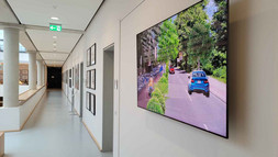 Das Bild zeigt die Radentscheid Ausstellung im Foyer des MIZ. Im Vordergrund ein Screen, auf dem eine Visualisierung zur Verkehrswende zu sehen ist.