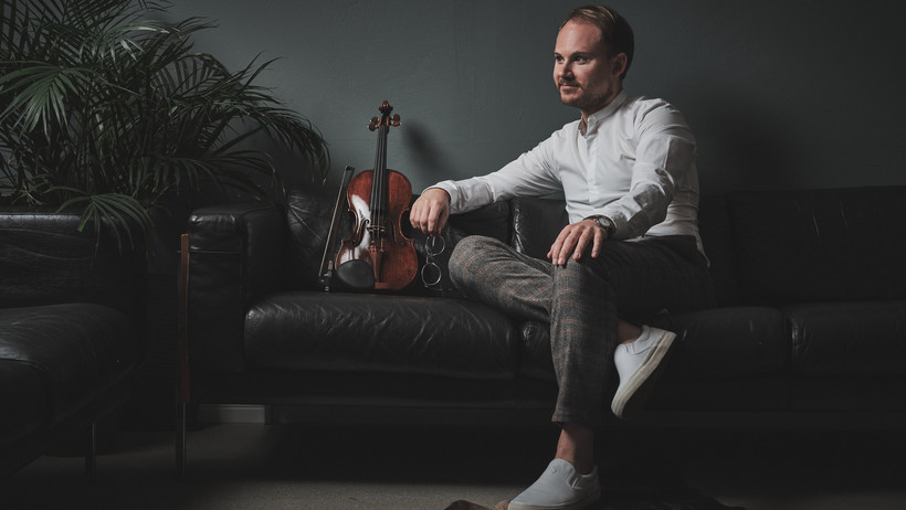 Niklas Liepe sitzt auf einem Sofa. Neben ihm eine Violine.