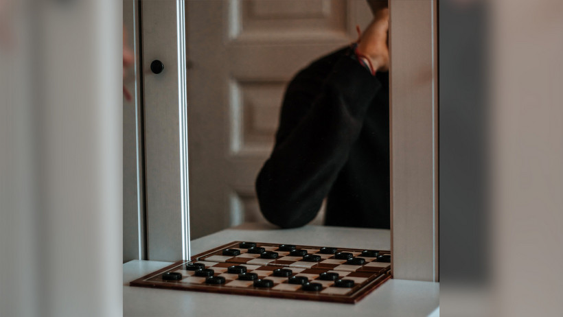 Das Bild zeigt ein Person im Spiegel, die gegen sich selbst Dame spielt