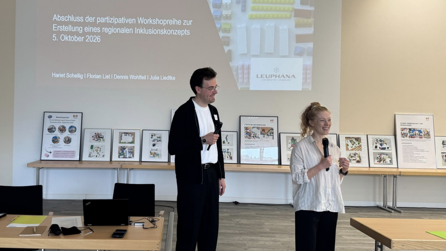 Zwei Menschen halten eine Präsentation, die im Hintergrund an die Wand projeziert wird.