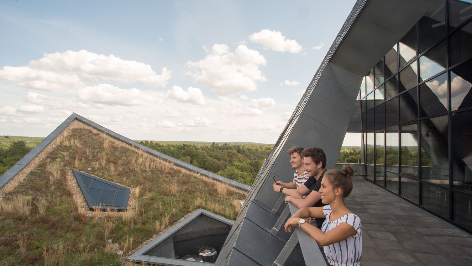 Three Spring School participants gaze into the distance from the balcony of the Leuphana central building.