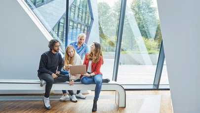 Four students looking a notebook screen in Leuphana's central building's entrance hall.