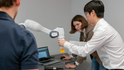 [Translate to Englisch:] Mitarbeitende der roboterfarik demonstrieren die einfache und gefahrlose Arbeit am Roboterarm