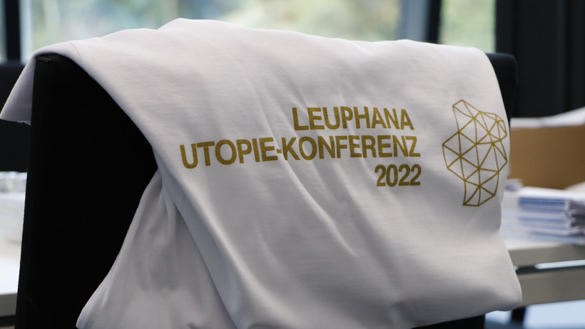 Ein weißes T-Shirt mit der Aufschrift "Utopie-Konferenz 2022" in gold