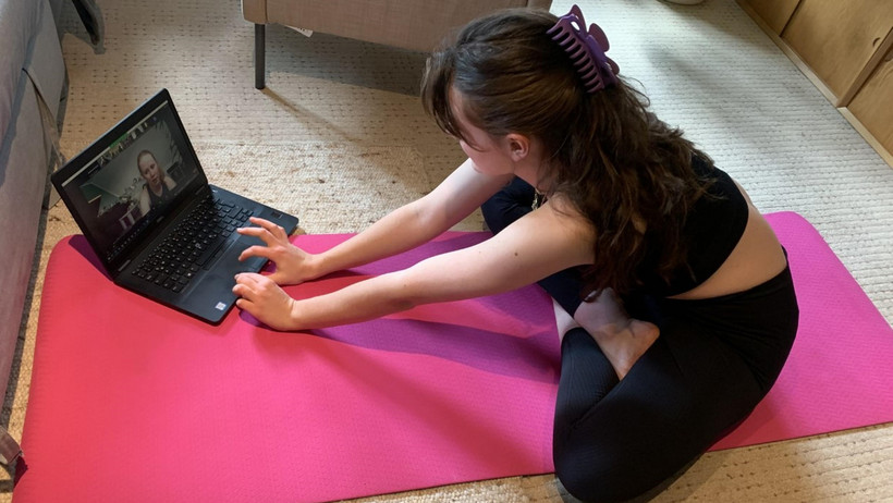 Eine Studierende auf einer Yoga Matte vor dem Laptop, auf dem die anderen Teilnehmer*innen zu sehen sind.